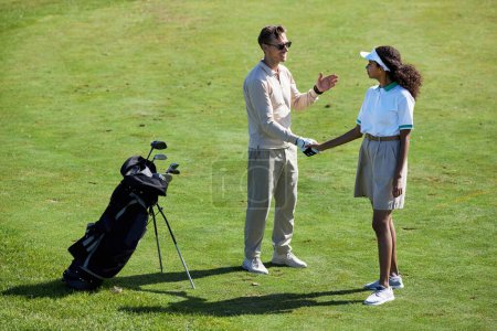 Téléchargez les photos : Portrait complet de deux joueurs de golf serrant la main sur le terrain vert après avoir apprécié le match - en image libre de droit