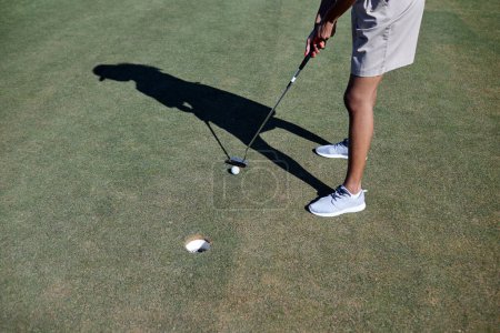 Téléchargez les photos : Minimal plan grand angle de la femme jouant au golf dans la lumière du soleil et visant balle au trou, copier l'espace - en image libre de droit