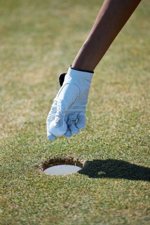 Téléchargez les photos : Gros plan vertical de la main gantée femelle ramassant la balle de golf du trou dans la lumière du soleil - en image libre de droit