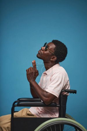 Téléchargez les photos : Portrait vertical latéral de jeune homme noir en fauteuil roulant sur fond bleu vif, minime - en image libre de droit