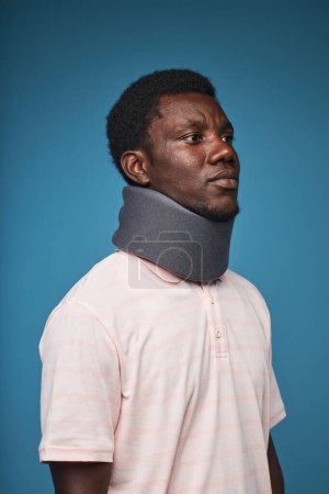 Téléchargez les photos : Portrait vertical de l'homme noir portant une attelle de cou sur fond bleu vif, minimal - en image libre de droit