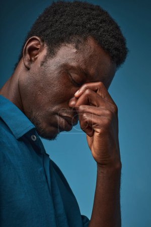 Foto de Retrato de vista lateral del hombre negro estresado con los ojos cerrados sobre fondo azul - Imagen libre de derechos