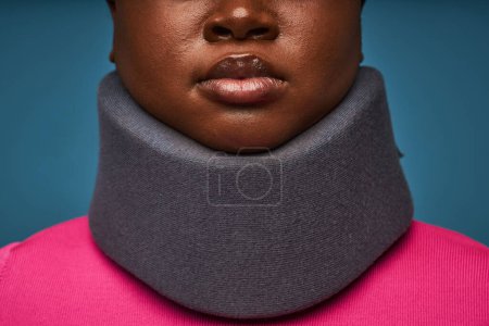 Téléchargez les photos : Gros plan minimal d'une femme noire méconnaissable portant une attelle de cou contre le bleu - en image libre de droit