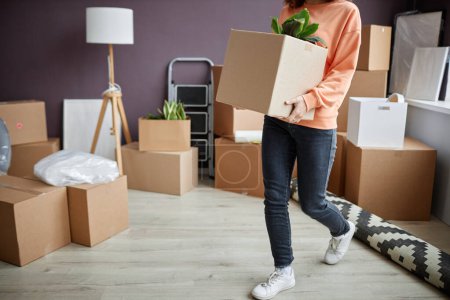Photo for Young woman holding cardboard box with things, she carrying them in her new apartment - Royalty Free Image