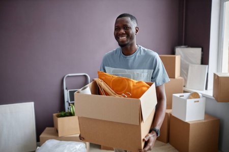 Photo for Happy African American man carrying cardboard boxes with things during relocation to a new house - Royalty Free Image