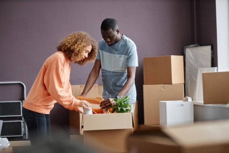 Photo for Young multiethnic couple packing things in cardboard boxes for moving to new house - Royalty Free Image