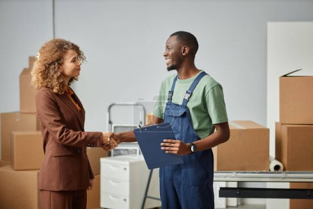 Photo for Young businesswoman concluding a deal with worker from moving service, they standing in office and shaking hands to each other - Royalty Free Image