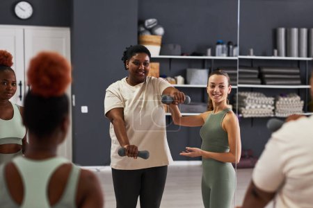 Téléchargez les photos : Jeune instructeur montrant des exercices avec haltères à la femme en surpoids pendant l'entraînement en classe - en image libre de droit