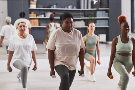 Téléchargez les photos : Groupe de femmes faisant de l'exercice avec des haltères ensemble pendant l'entraînement sportif en salle de gym - en image libre de droit