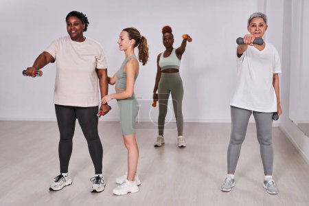 Téléchargez les photos : Femmes multiethniques faisant de l'exercice avec des haltères avec un instructeur dans une salle de gym - en image libre de droit