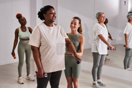 Téléchargez les photos : Jeune instructeur de formation des femmes dans le club de santé, ils font des exercices avec haltères - en image libre de droit