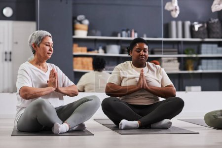 Téléchargez les photos : Femmes assises en position lotus et méditant les yeux fermés pendant l'entraînement sportif dans un club de santé - en image libre de droit