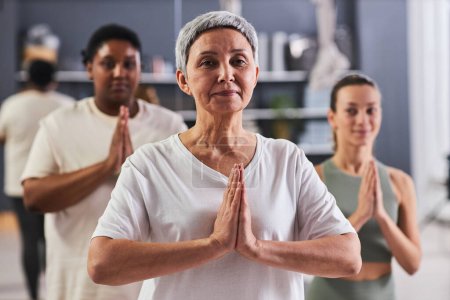 Photo for Portrait of mature woman looking at camera while doing yoga in class with other women in background - Royalty Free Image