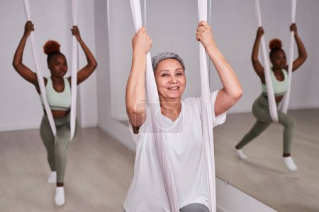 Foto de Retrato de mujer madura sonriendo a cámara mientras hace aero yoga en club de salud - Imagen libre de derechos