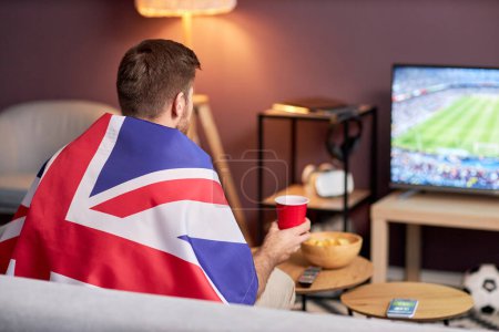 Foto de Vista trasera de los fanáticos de los deportes con bandera del Reino Unido mientras ve el partido de fútbol en casa, espacio de copia - Imagen libre de derechos