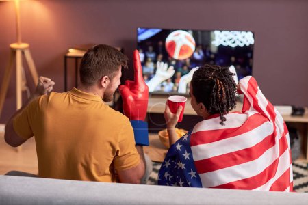 Téléchargez les photos : Vue arrière de deux fans de sport excités regardant le match de basket à la maison et acclamant - en image libre de droit