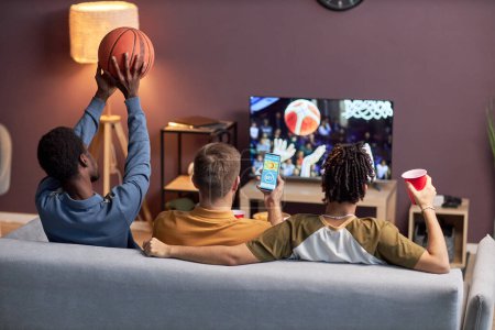 Téléchargez les photos : Vue arrière du groupe d'amis regardant le match de basket à la maison et buvant de la bière - en image libre de droit
