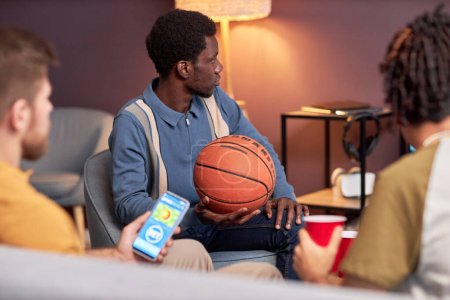 Téléchargez les photos : Vue latérale à divers groupes de fans de sport regarder le match de basket à la maison et en utilisant l'application de paris en ligne - en image libre de droit