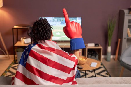 Téléchargez les photos : Vue arrière au drapeau de fan de sport tout en regardant le match de baseball à la télévision à la maison et en acclamant - en image libre de droit