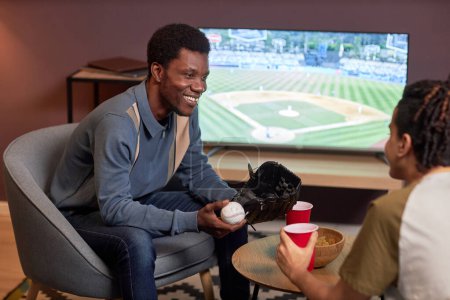 Foto de Retrato de dos amigos discutiendo partido de béisbol en casa y sonriendo alegremente - Imagen libre de derechos