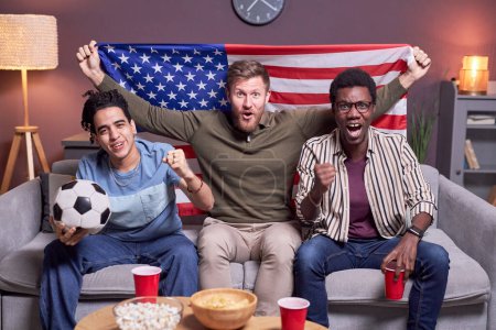 Foto de Diverso grupo de fanáticos de los deportes viendo el partido en la televisión en casa y ondeando la bandera de EE.UU. - Imagen libre de derechos
