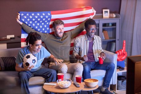 Téléchargez les photos : Groupe diversifié de fans de sport regardant le match de football à la maison et acclamant éclairé par la lumière bleue - en image libre de droit