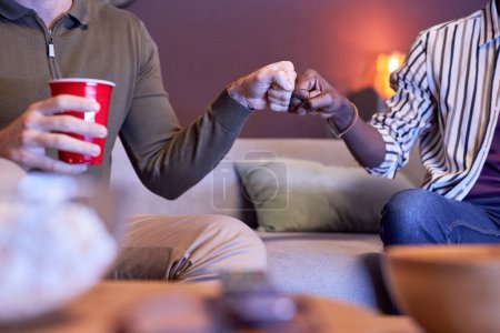 Foto de Primer plano de dos amigos golpe de puño mientras ve la televisión en casa en luz azul - Imagen libre de derechos