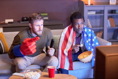 Téléchargez les photos : Portrait de deux amis regardant un match de sport à la maison avec le drapeau américain éclairé par la lumière bleue - en image libre de droit
