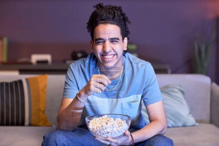 Foto de Retrato de un hombre mirando televisión en casa con luz azul y comiendo palomitas de maíz, espacio para copiar - Imagen libre de derechos