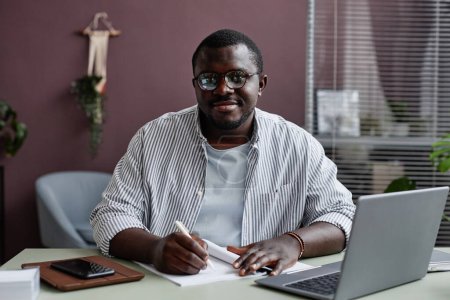 Téléchargez les photos : Portrait de l'homme noir souriant portant des lunettes sur le lieu de travail au bureau - en image libre de droit