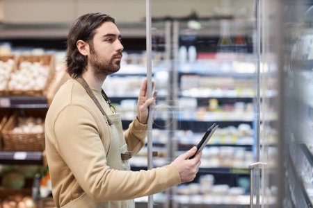 Foto de Retrato de vista lateral del trabajador masculino en el supermercado que revisa el inventario de productos lácteos - Imagen libre de derechos