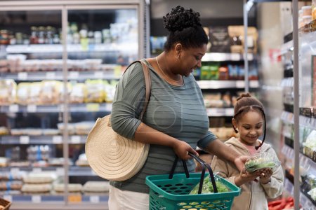 Photo for Portrait of mother shopping in supermarket with little daughter and buying vegetables - Royalty Free Image