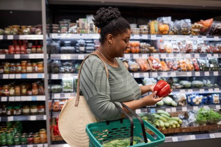 Téléchargez les photos : Portrait latéral d'une femme noire souriante faisant ses courses au supermarché et achetant des légumes frais - en image libre de droit