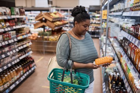 Photo for Portrait of black young woman choosing dairy products while grocery shopping in supermarket - Royalty Free Image