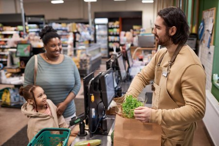 Photo for Side view portrait of smiling male worker in supermarket helping young woman with groceries - Royalty Free Image