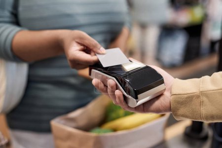 Téléchargez les photos : Gros plan d'une femme noire méconnaissable payant par carte de crédit dans un supermarché et achetant des produits d'épicerie, espace de copie - en image libre de droit