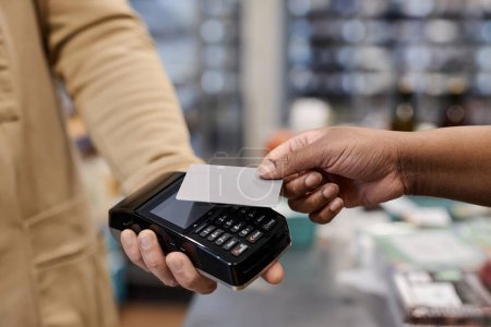 Téléchargez les photos : Gros plan d'une femme noire méconnaissable payant via NFC et tenant une maquette de carte de crédit dans un supermarché, espace de copie - en image libre de droit