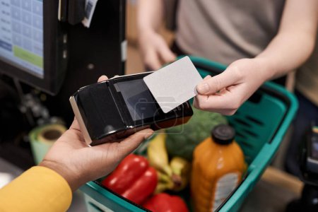 Téléchargez les photos : Jeune femme méconnaissable utilisant la maquette de carte de crédit payer pour les épiceries dans un supermarché, espace de copie - en image libre de droit