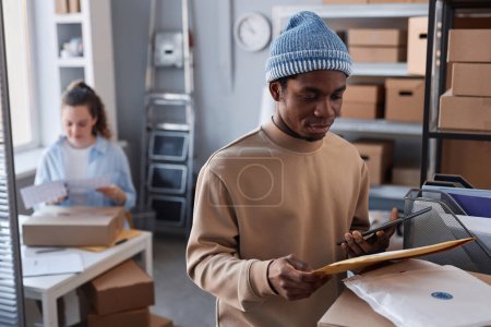 Photo for Young male worker of post office revising numbers of packets and parcels and checking them in tablet against female colleague - Royalty Free Image