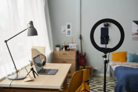 Foto de Marco redondo con smartphone en soporte de pie contra el lugar de trabajo del diseñador, freelancer o estudiante con lámpara sobre portátil en el dormitorio - Imagen libre de derechos