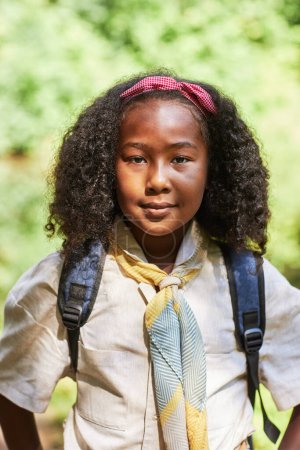 Téléchargez les photos : Portrait vertical de la fille noire mignonne comme éclaireuse portant l'uniforme en plein air dans la forêt - en image libre de droit