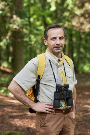 Foto de Retrato vertical del hombre adulto como líder scout mirando a la cámara al aire libre en el bosque y usando equipo de senderismo - Imagen libre de derechos