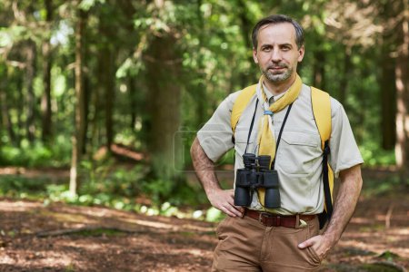 Téléchargez les photos : Portrait taille haute de l'homme adulte comme chef scout regardant la caméra à l'extérieur dans la forêt et souriant, espace de copie - en image libre de droit