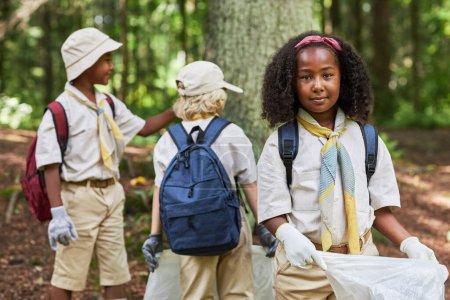 Foto de Cintura hacia arriba retrato de linda chica negra como scout ayudando a limpiar el bosque y la celebración de la bolsa de basura, espacio de copia - Imagen libre de derechos