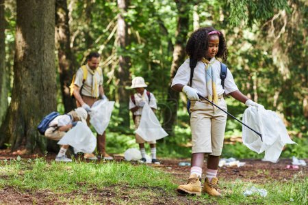 Téléchargez les photos : Portrait complet de fille noire mignonne comme éclaireur de fille aidant à nettoyer la forêt et tenant sac poubelle, espace de copie - en image libre de droit