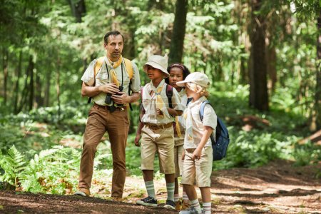 Foto de Vista completa en diverso grupo de exploradores caminando en el bosque con líder adulto, espacio de copia - Imagen libre de derechos