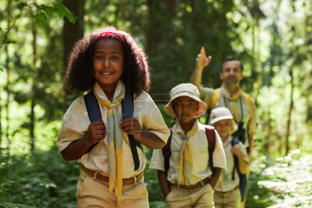 Foto de Cintura hacia arriba retrato de chica negra con grupo de exploradores caminando en el bosque y sonriendo a la cámara, espacio de copia - Imagen libre de derechos