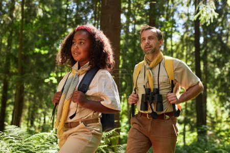 Photo for Waist up portrait of cute girl scout hiking in forest with adult leader scene lit by sunlight - Royalty Free Image