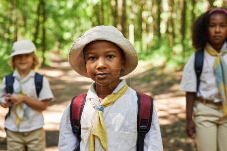 Téléchargez les photos : Portrait taille haute de jeune garçon noir comme boy scout portant l'uniforme à l'extérieur dans la forêt - en image libre de droit