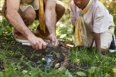 Foto de Primer plano del hombre adulto como líder scout teching niño pequeño iniciando fogata en el bosque - Imagen libre de derechos